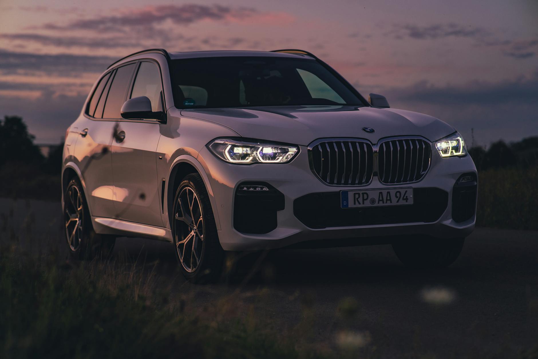 Białe SUV BMW zaparkowane o zmierzchu na tle spokojnego krajobrazu