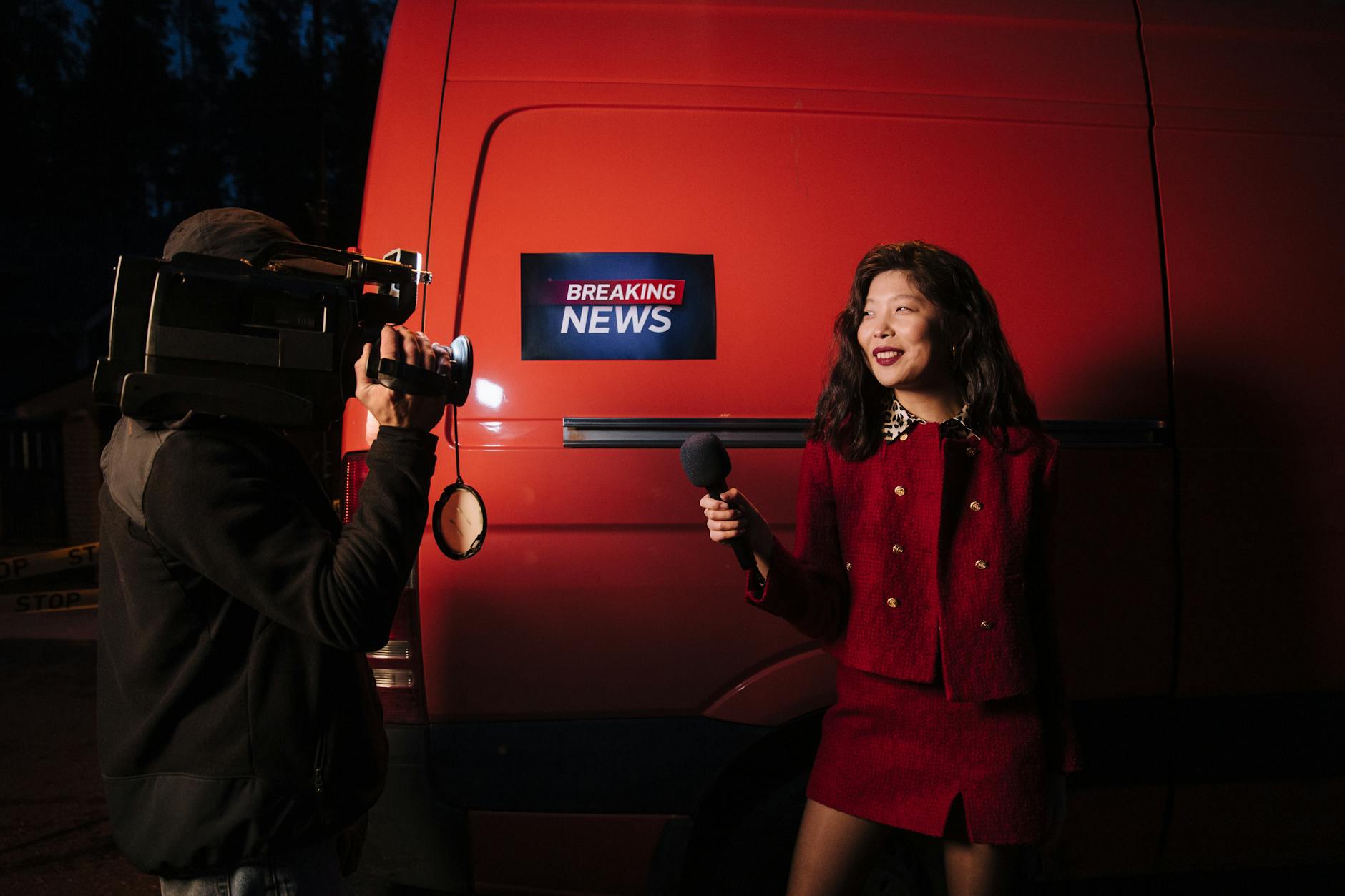 Reporter z mikrofonem przy czerwonym aucie podczas nocnego nagrania