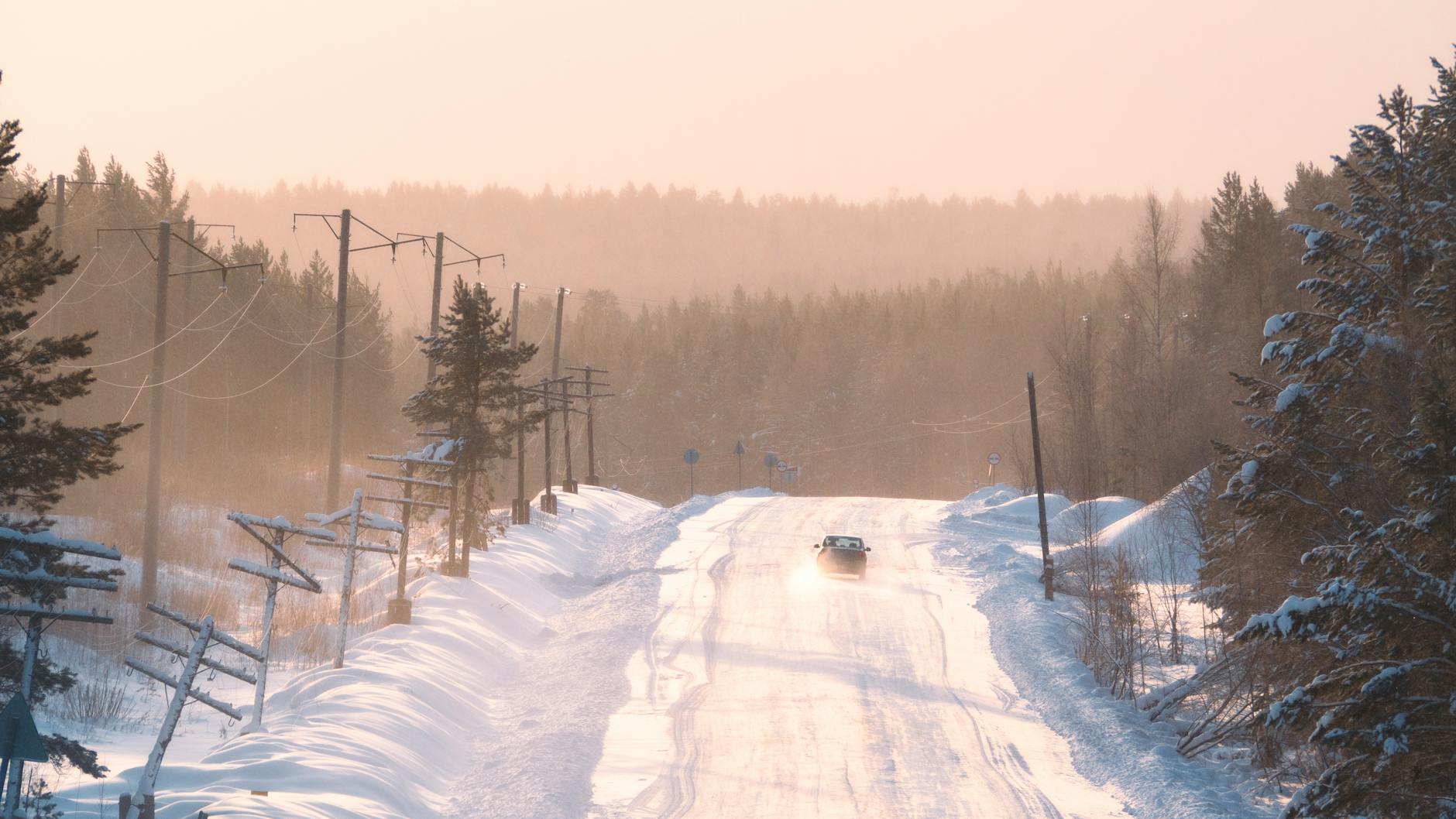 Samochód na ośnieżonej drodze o zachodzie słońca zimą