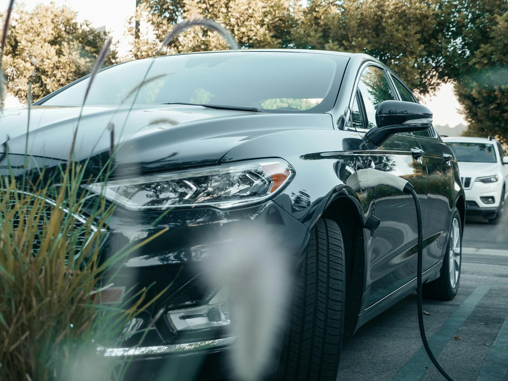 Czarny samochód elektryczny Tesla ładowany przy stacji w zielonym otoczeniu
