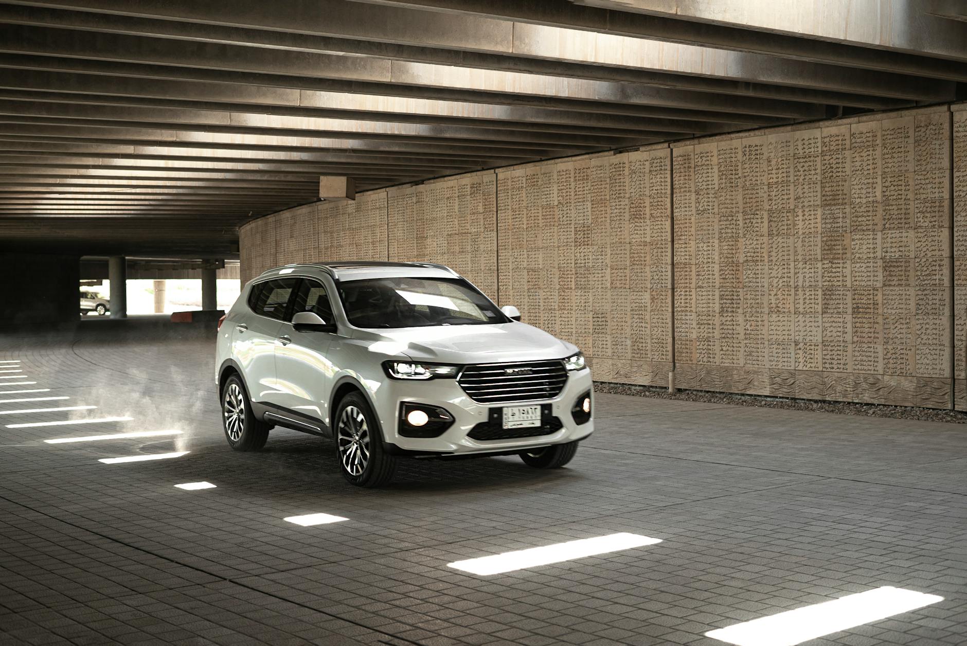 Srebrny Cadillac Escalade jedzie pod betonową estakadą