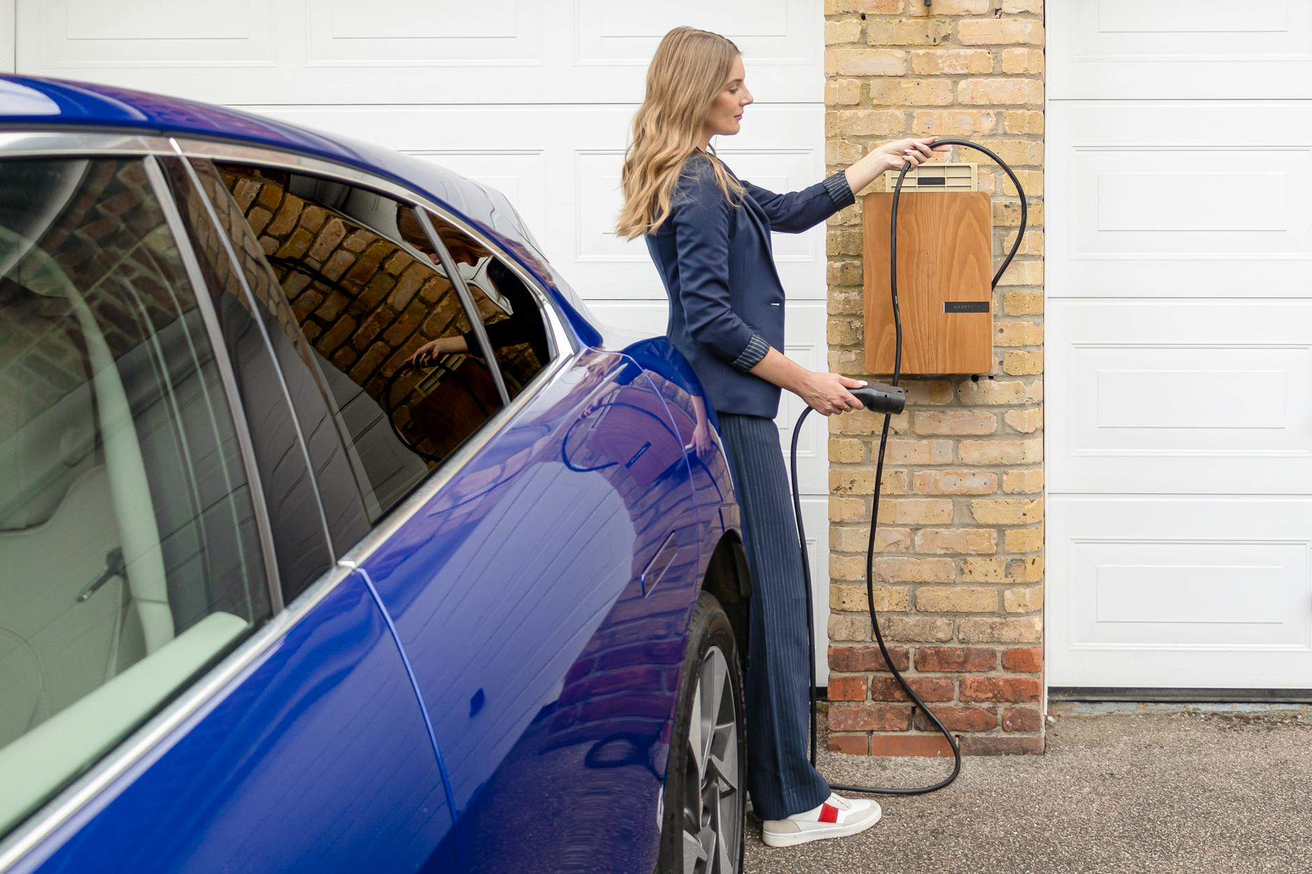 Kobieta ładuje niebieską Dacię Spring przy domowej ładowarce EV